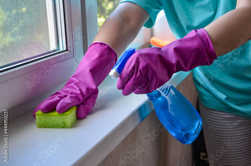Washing windows. Female hands in gloves hold spray bottle with glass cleaner and sponge. woman washes window and sill in apartment. Hands in gloves close up. Household chemicals, house cleaning