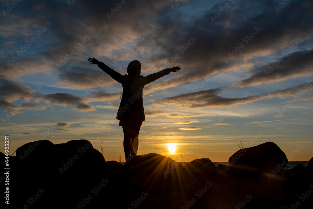 Silhouette of a young girl with hands raised up against the background of the evening sky. World perception concept.