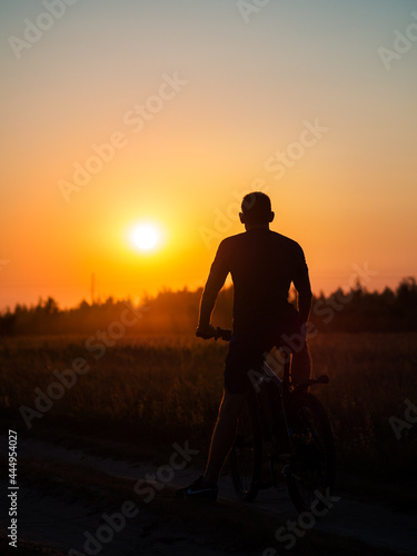 The silhouette of a cyclist at sunset in a field. Cycling on a summer evening