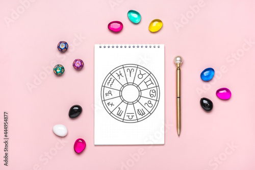 Horoscope circle with twelve signs of zodiac on paper, divination dice, colorful stone on pink background Fortune telling and astrology predictions Top view Flat lay