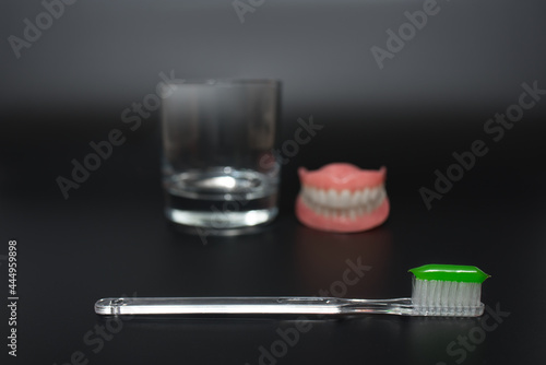 Full removable plastic denture of the jaws. Two acrylic dentures. Dental care with an toothbrush. Teeth and toothbrush on a dark background. Dental prosthesis care. Oral hygiene. Copy space.