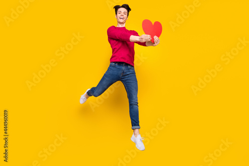 Full body photo of funky brunet millennial guy jump give heart wear red sweater jeans isolated on yellow color background © deagreez