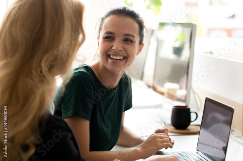 Happy millennial intern, student girl talking to teacher, consulting tutor, mentor at computer in training center, discussing new professional skills, smiling, laughing. Business education, internship photo