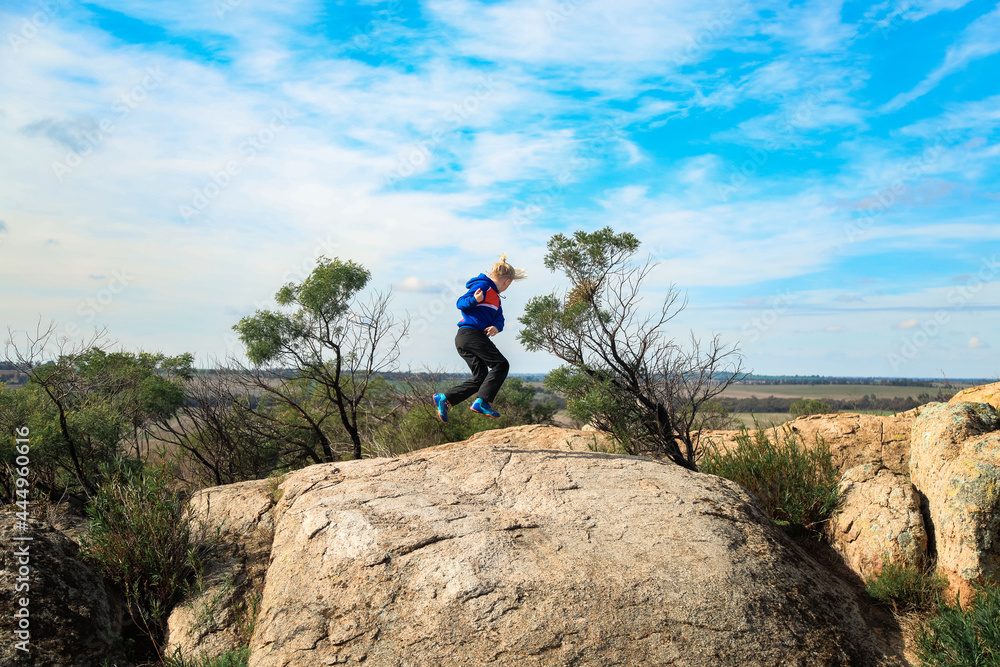 Blonde boy jumping on rock in nature with large sweeping view in background