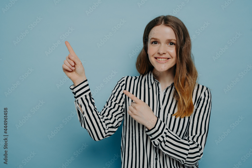 Smiling young woman pointing up with two forefingers up and with happy face expression Smiling young woman pointing up with two forefingers up and with happy face expression