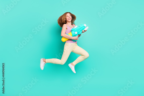 Full length body size photo girl jumping up with water blaster in summer isolated vibrant teal color background
