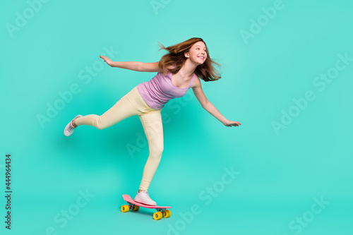 Fototapeta Naklejka Na Ścianę i Meble -  Full length body size photo girl riding on longboard looking copyspace in summer isolated vivid teal color background