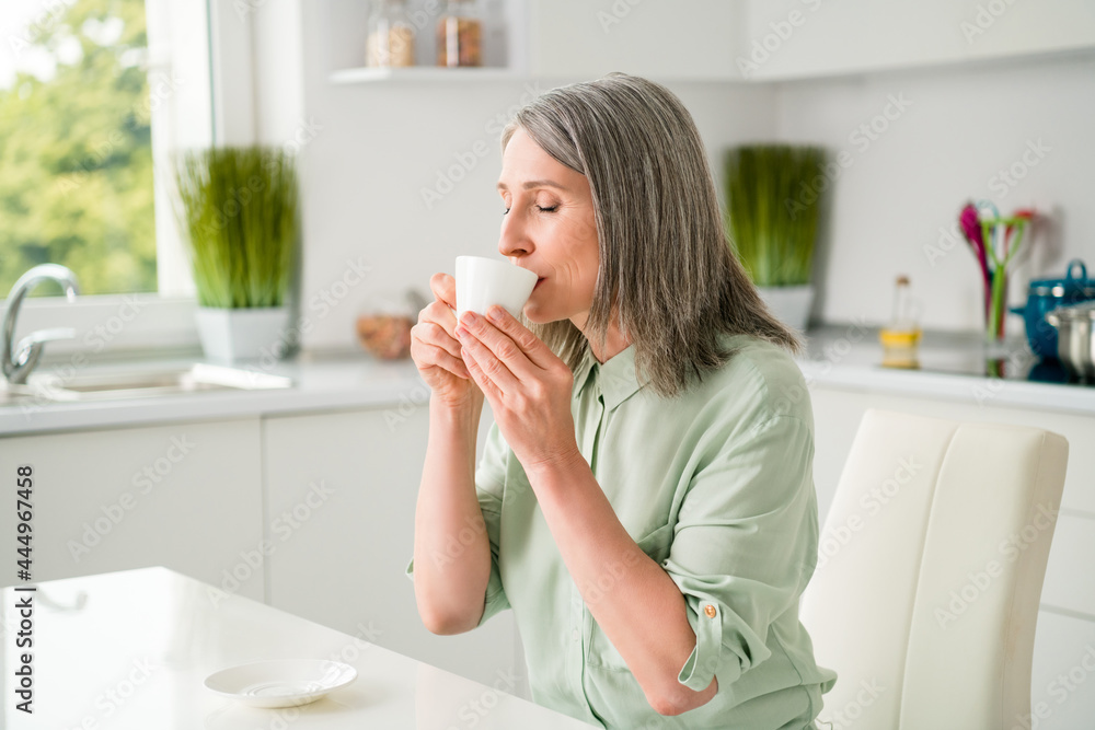 Profile side view portrait of attractive dreamy calm peaceful grey-haired woman drinking espresso alone at home light white indoors Profile side view portrait of attractive dreamy calm peaceful grey-haired woman drinking espresso alone at home light white indoors