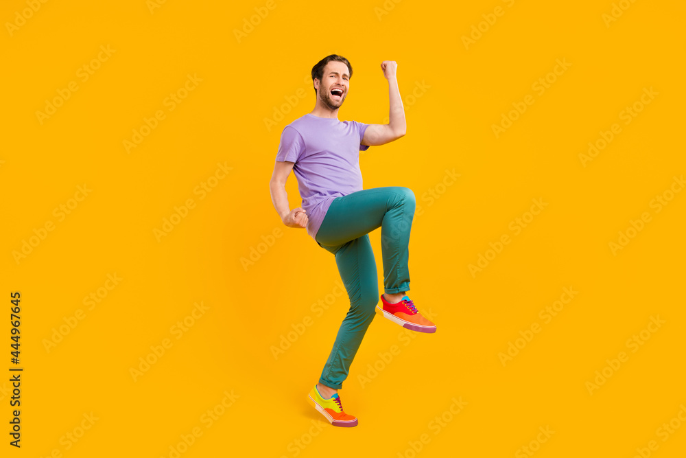 Photo of astonished lucky guy celebrate victory wear purple t-shirt pants sneakers isolated yellow color background