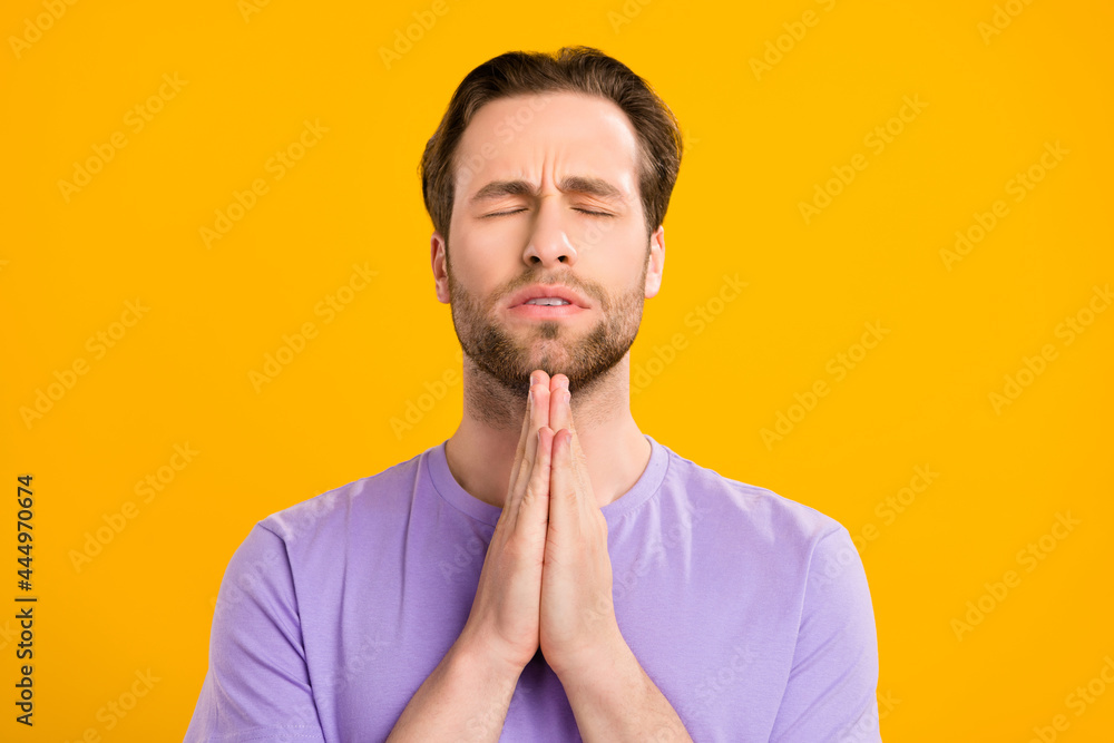 Photo of pretty nervous young guy dressed purple t-shirt arms together closed eyes praying isolated yellow color background Photo of pretty nervous young guy dressed purple t-shirt arms together closed eyes praying isolated yellow color background