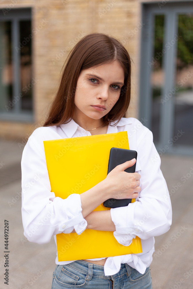 Upset girl student with a folder outdoors. Bullying at the university. Public humiliation. Upset girl student with a folder outdoors. Bullying at the university. Public humiliation.