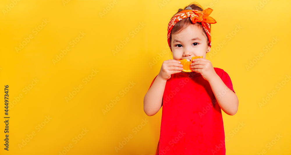 a beautiful little girl in a red T-shirt and an orange bandana eats a slice of orange on a yellow background