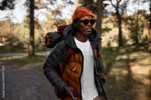 Afro american guy walking alone on forest trail. Hiking with sleeping bag. Exploring virgin nature, looking for new adventures and experience. Travelling and exploring world concept