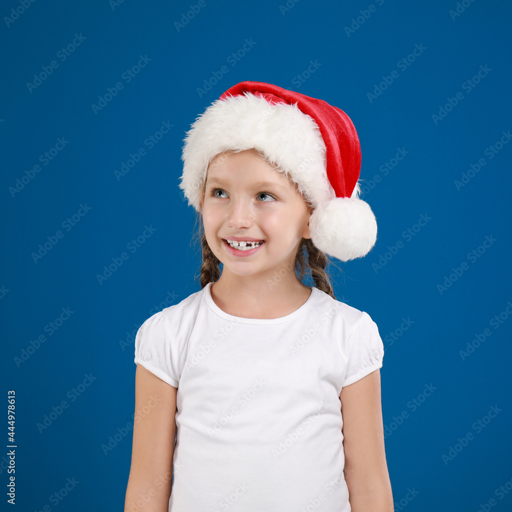 Happy little child in Santa hat on blue background. Christmas celebration