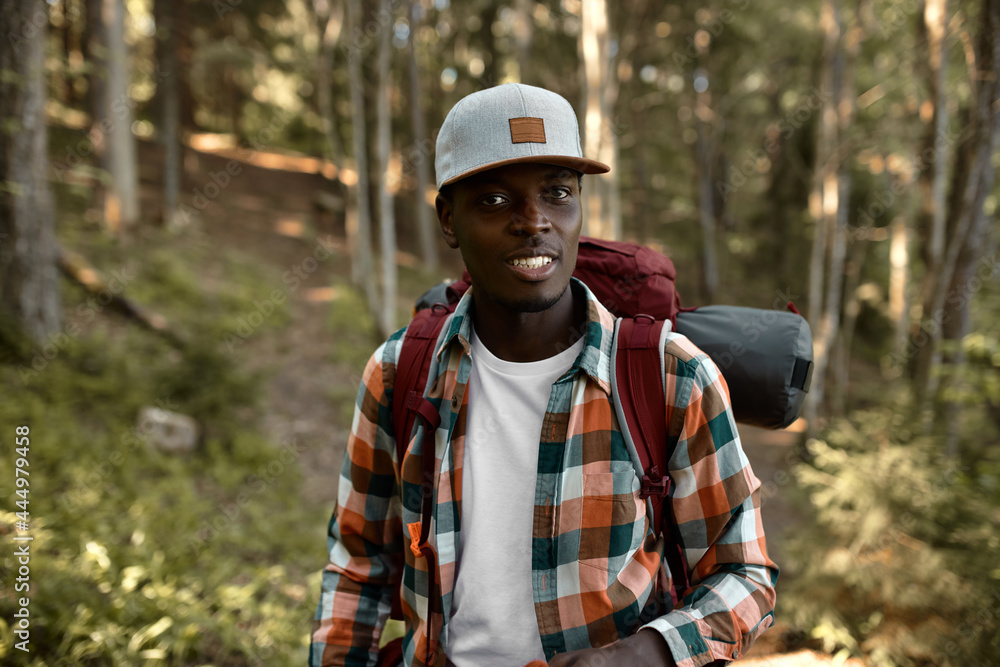 Adventurous afro american man ready for long forest hiking. Stylish guy in cap all alone enjoying nature vibes. Summer journey, find adventure, camping in nature, travelling concept Adventurous afro american man ready for long forest hiking. Stylish guy in cap all alone enjoying nature vibes. Summer journey, find adventure, camping in nature, travelling concept