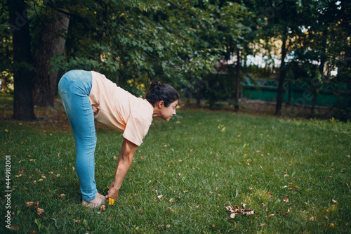 Indian woman in ordinary casual clothes doing yoga in outdoor summer park.