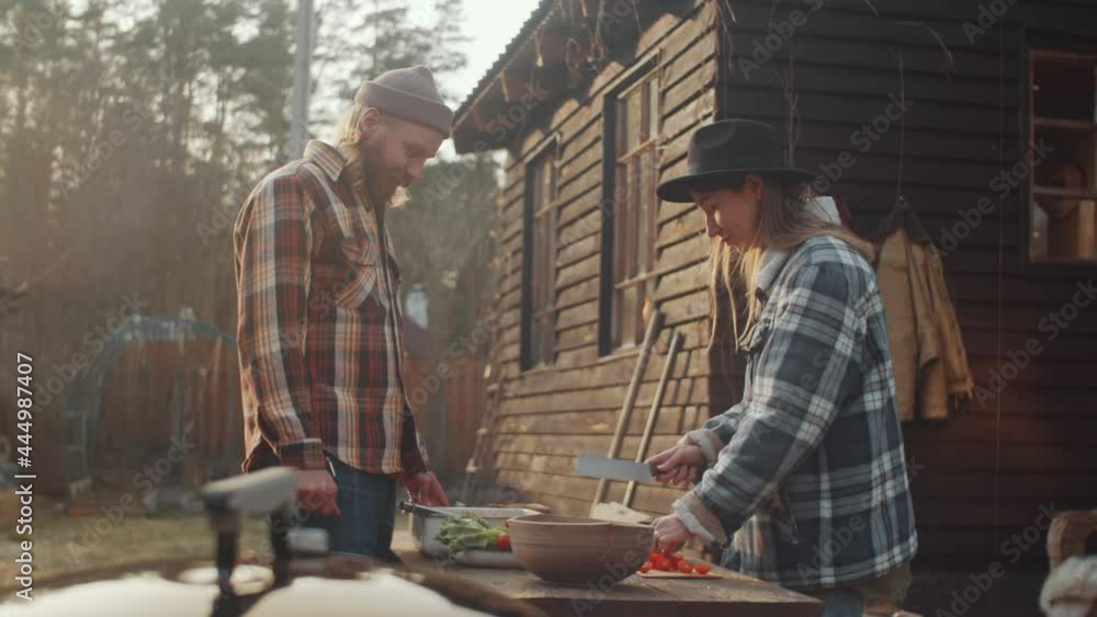 Young man and woman cutting vegetables and preparing meat before cooking food on barbecue in backyard of farmhouse Young man and woman cutting vegetables and preparing meat before cooking food on barbecue in backyard of farmhouse