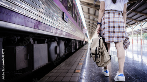 Young woman traveler with backpack walking at train station and waits train on railway platform. Travel concept.