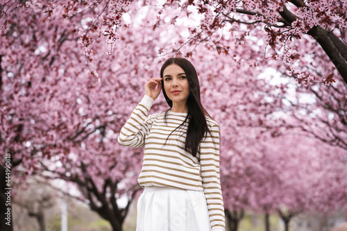 Pretty young woman in park with blooming trees. Spring look
