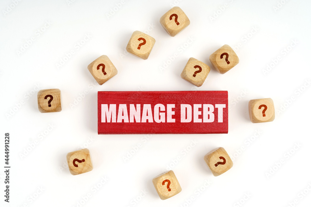 On the table are cubes with questions and a red plaque with the inscription - Manage Debt On the table are cubes with questions and a red plaque with the inscription - Manage Debt
