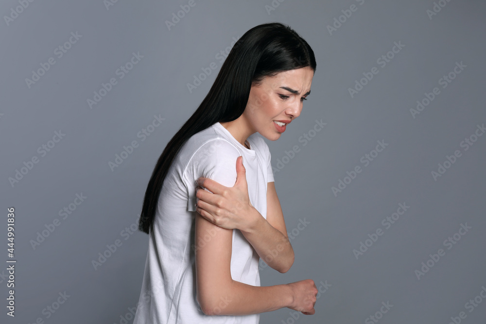 Woman suffering from shoulder pain on grey background Woman suffering from shoulder pain on grey background