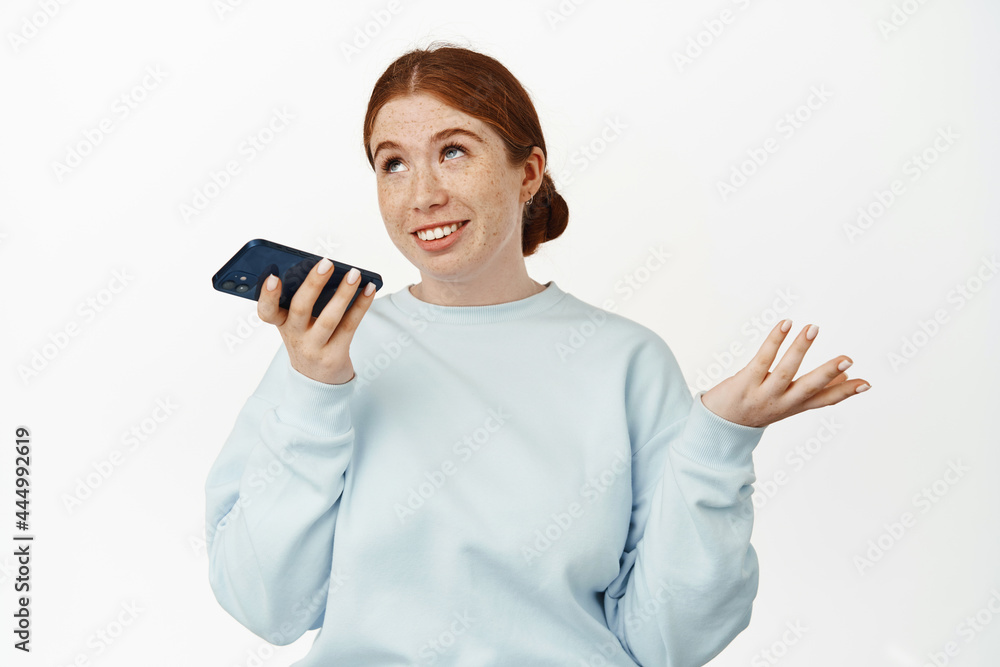 Image of redhead caucasian girl record voice message, talking on speakerphone, gesturing and chatting on mobile app, smiling relaxed, white background Image of redhead caucasian girl record voice message, talking on speakerphone, gesturing and chatting on mobile app, smiling relaxed, white background