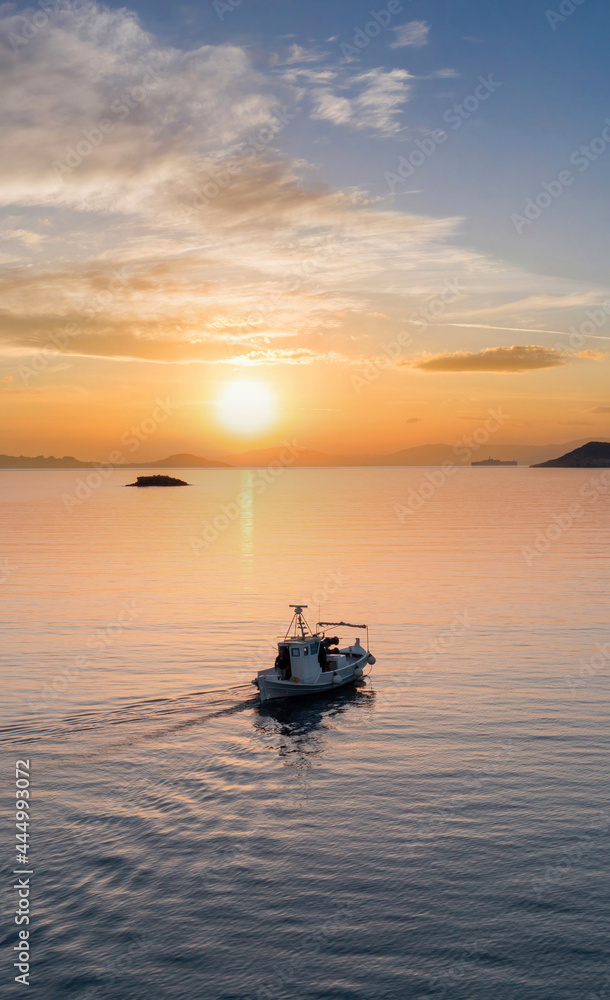 Fishing boat at sunset. Greece. Aerial drone view of typical fishing boat moving on calm sea and orange color sky background.