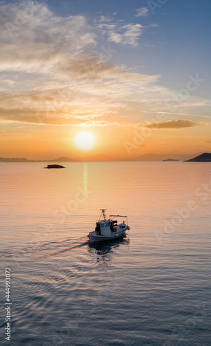 Fishing boat at sunset. Greece. Aerial drone view of typical fishing boat moving on calm sea and orange color sky background.
