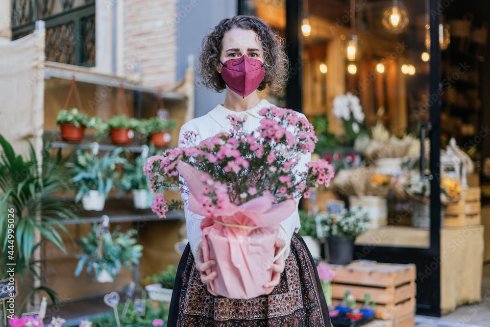 Young girl with mask showing a pot with plants in front of a flower store. Focus on the face. Young girl with mask showing a pot with plants in front of a flower store. Focus on the face.