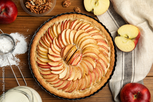 Delicious homemade apple tart and ingredients on wooden table, flat lay