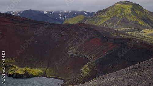 Amazing Icelandic nature. Red and black crater with colourful mountain in the background. Green and snowy hills with crater full of iron and emerald colour lake in the mystic foggy weather. photo