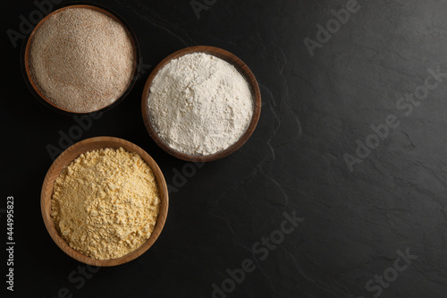 Different types of flours on black table, flat lay. Space for text