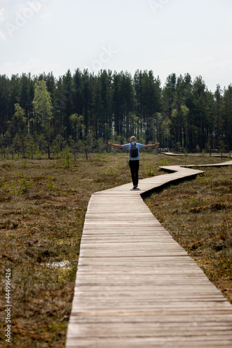 man in a light shirt walking on a wooden path in nature  national park or forest  swamp and wooden roads for hiking and walking  recreation and sports in nature  enjoy the peace and beauty  treveler
