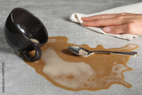 Woman wiping spilled coffee on grey table, closeup photo