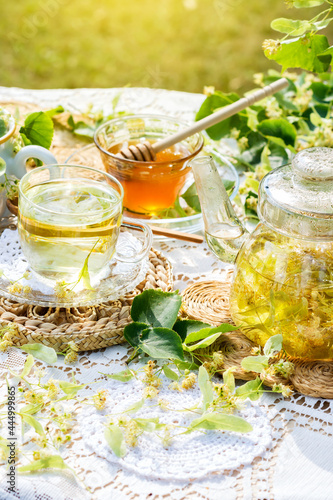 Linden flowers tea in a glass cup and teapot on a white napkin, on a white tablecloth background, yellow drink of linden flower with linden blossoms honey in nature background