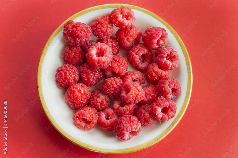 Ripe organic raspberry berry on plate, healthy pile of summer berries top view. Pattern flat lay of scarlet raspberry on red background Ripe organic raspberry berry on plate, healthy pile of summer berries top view. Pattern flat lay of scarlet raspberry on red background