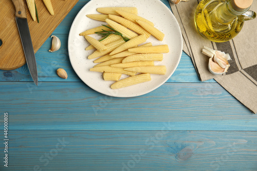 Fresh baby corn cobs on blue wooden table, flat lay. Space for text