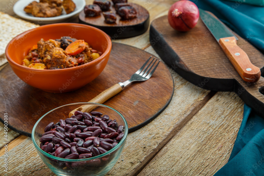 Jewish dish chelnt with meat in a plate on a wooden table on a stand next to ingredients. Jewish dish chelnt with meat in a plate on a wooden table on a stand next to ingredients.
