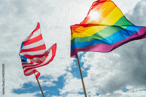 low angle view of american and colorful lgbt flags against blue sky with clouds