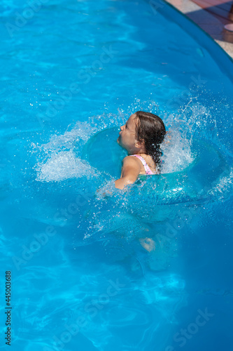 a five-year-old girl jumps into the water from the edge of the pool sending splashes and drops of water in all directions. 