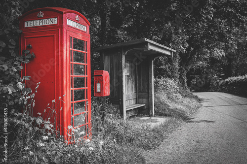 Traditional red British telephone booth, post box and wooden bus stop, selective color on black and white background, no people. Wales, UK photo