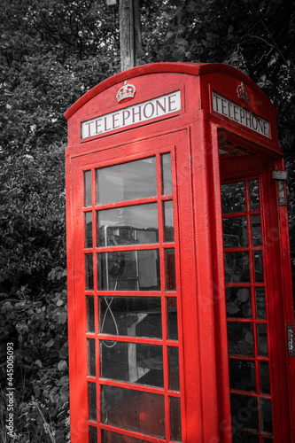 Traditional old red telephone box  selective color  close-up. Vintage British phone booth on black and white tree background.