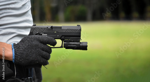 Automatic 9mm pistol which has flashlight under the muzzle holding in hand and ready to shoot, natural blurred background.