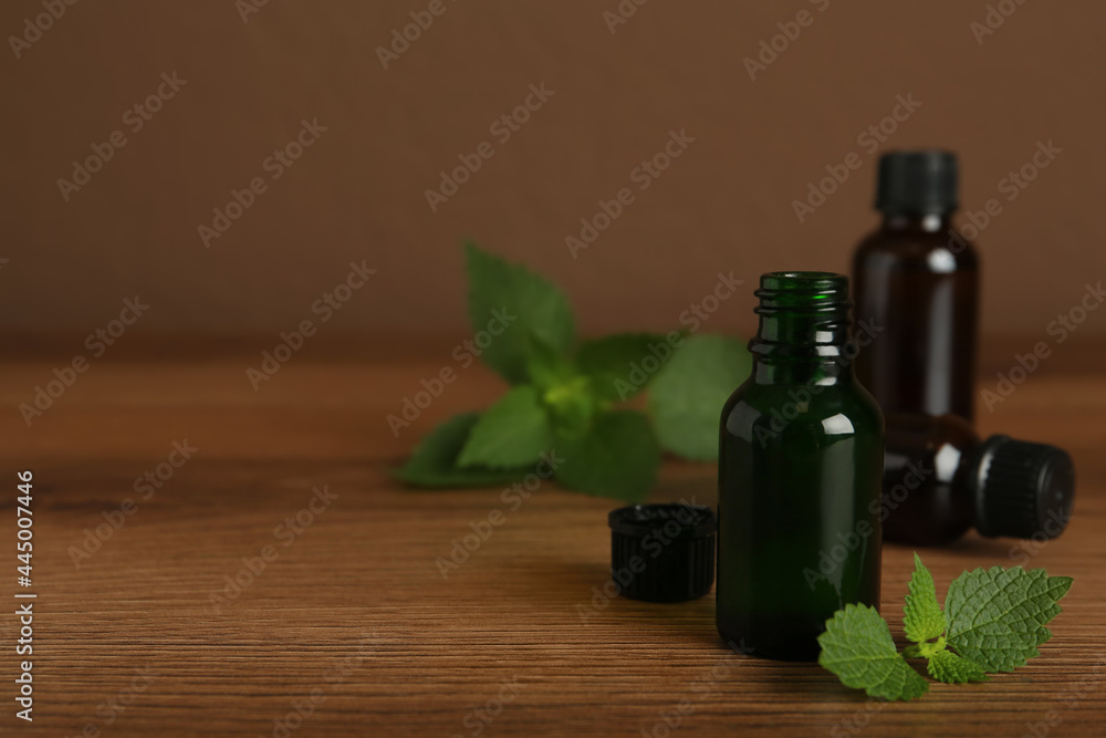 Glass bottles of nettle oil and leaves on wooden table against brown background, space for text Glass bottles of nettle oil and leaves on wooden table against brown background, space for text