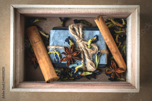 A block of natural carbon soap in a wooden box with cinnamon sticks.
