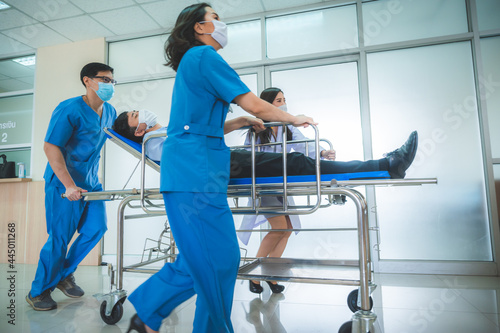 a group of medics or doctors carrying male patient on hospital gurney to emergency or operation room, urgent caseon  gurney being pushed at speed through a hospital.