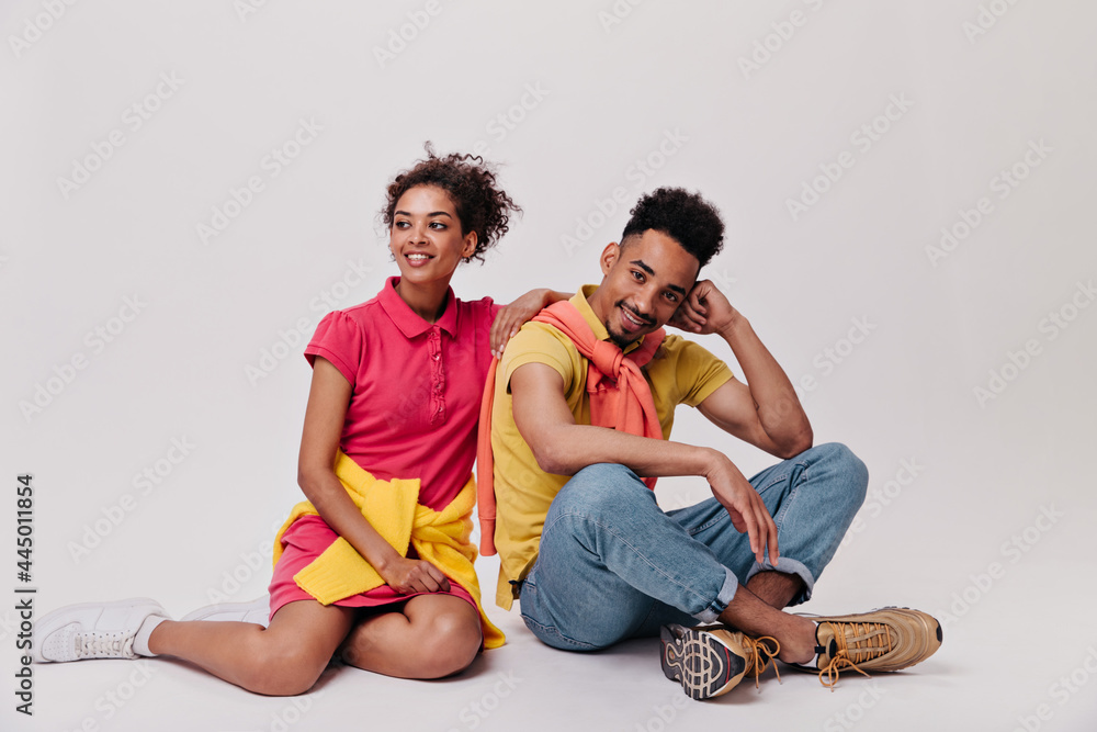 Good looking man and his girlfriend sitting on white background. Portrait of handsome guy in jeans and brunette woman in red dress Good looking man and his girlfriend sitting on white background. Portrait of handsome guy in jeans and brunette woman in red dress