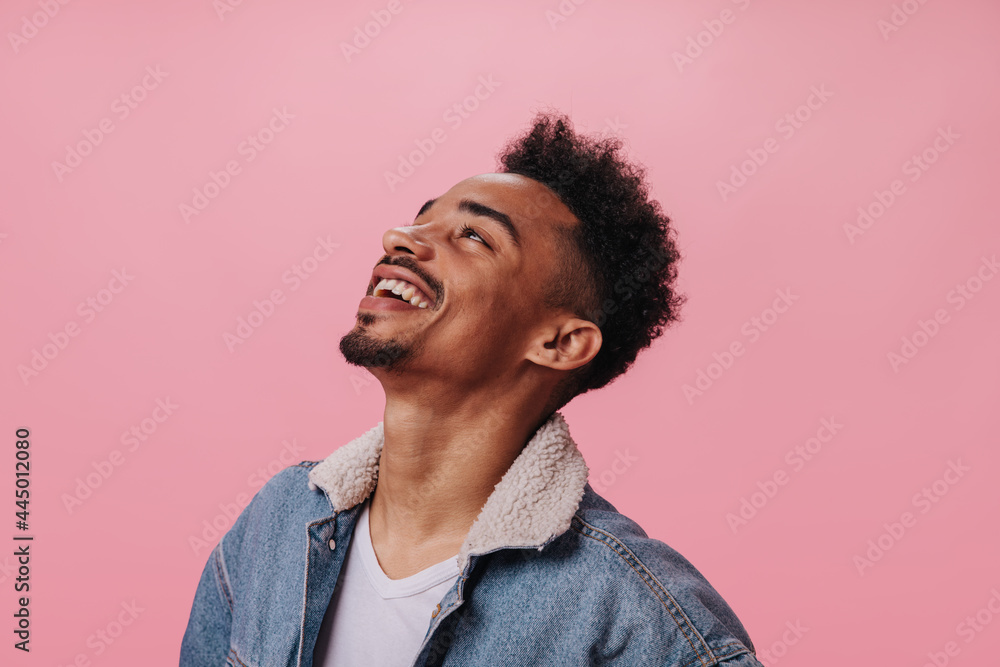 Happy man in denim outfit smiling on pink background. Cheerful brunette guy in white t-shirt laughing on isolated backdrop - obrazy, fototapety, plakaty 