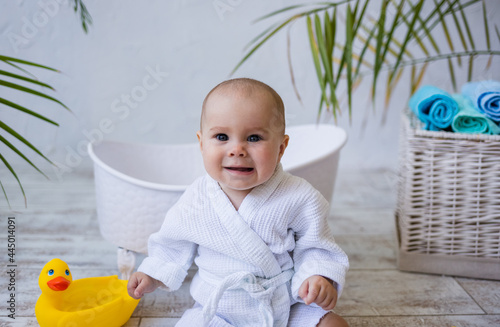 portrait of a baby girl in a white robe sitting near a bath on a white background with a place for text. Child care