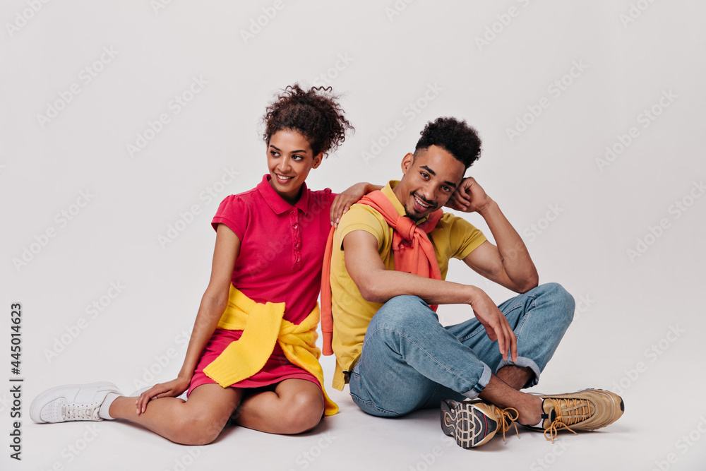 Charming lady and her boyfriend sit on white background. Pretty brunette girl in red dress and man in jeans pose on isolated backdrop Charming lady and her boyfriend sit on white background. Pretty brunette girl in red dress and man in jeans pose on isolated backdrop